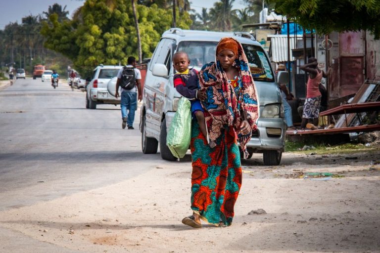 A mother and child walk together in a vibrant street scene in Zanzibar, Tanzania.
